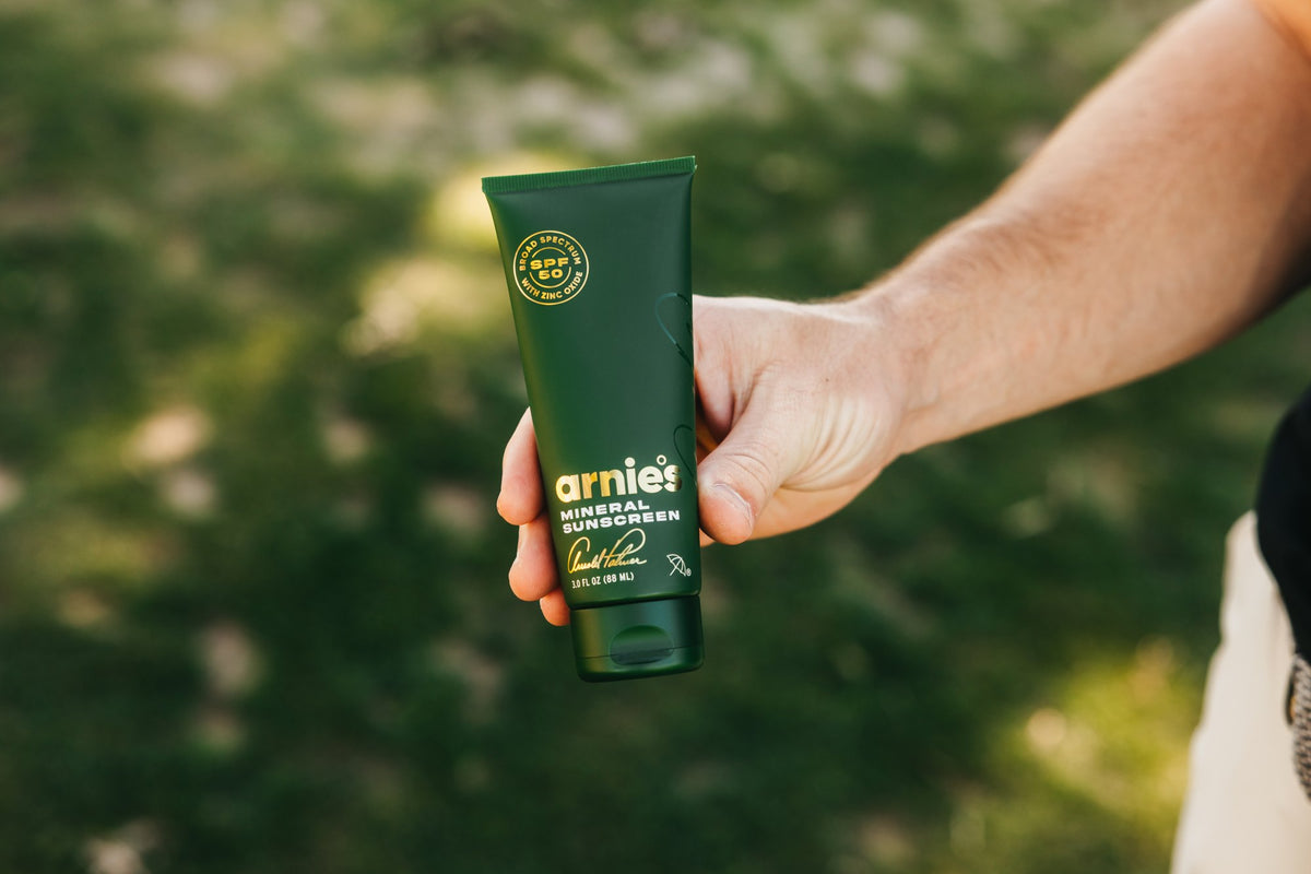 A golfer holding Arnie's Mineral Face Sunscreen outdoors.