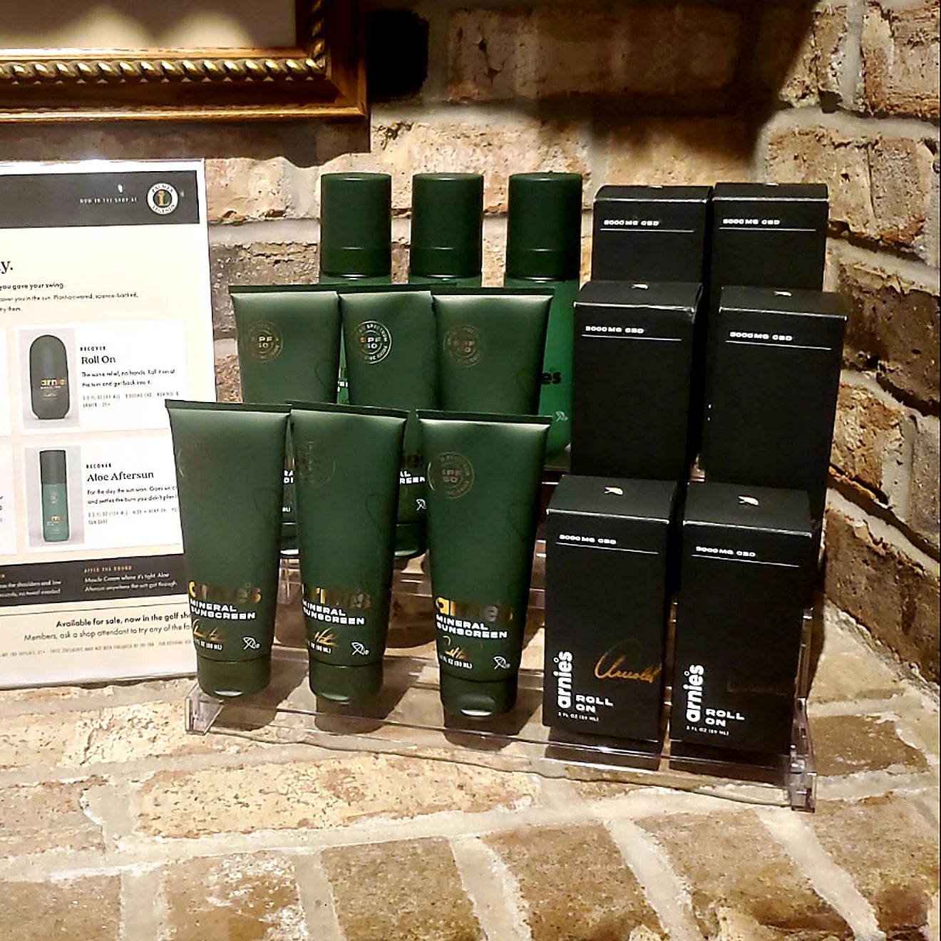 Arnie's Mineral Face Sunscreen, Muscle Cream and Roll On on an acrylic riser beside the Arnie's counter card in the pro shop at Palmer Legends Country Club
